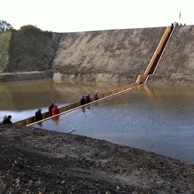 Visitors walking through water on the almost invisible Moses Bridge at Fort de Roovere.