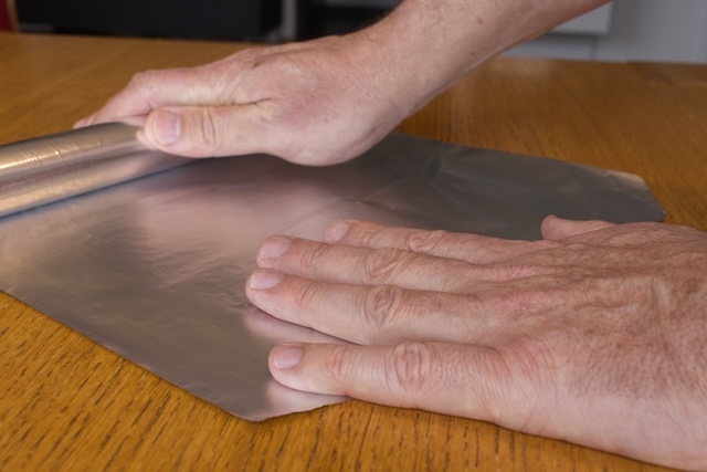 A piece of aluminum foil being prepared, showcasing how easily available materials can be used to improve Wi-Fi performance by reflecting and focusing the signal.