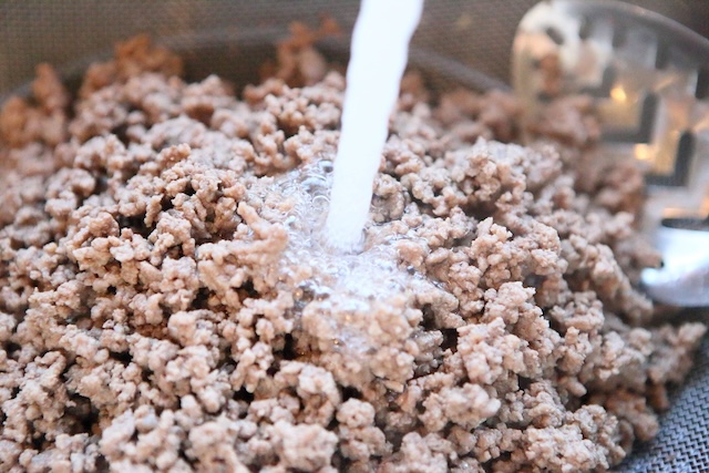 Some cooks rinse their ground beef after browning, believing it removes excess fat and potential bacteria, as shown in this image of rinsed beef under running water