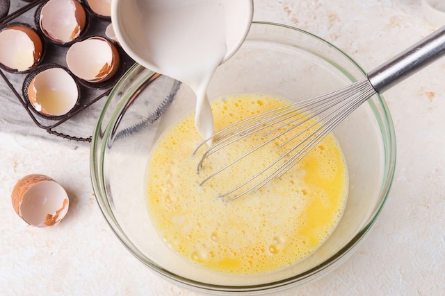 Milk being added to whisked eggs, a common but debated practice in many kitchens. Does it enhance the eggs' creaminess, or does it water down the flavor?