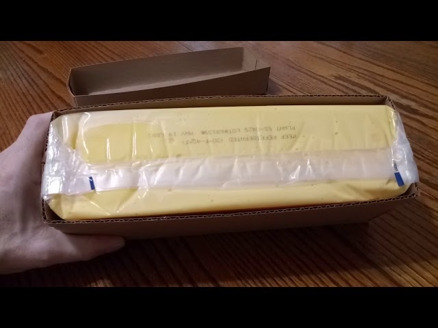 A closer look at a block of government cheese, packaged in cardboard and plastic, ready to be used in countless meals by families across America