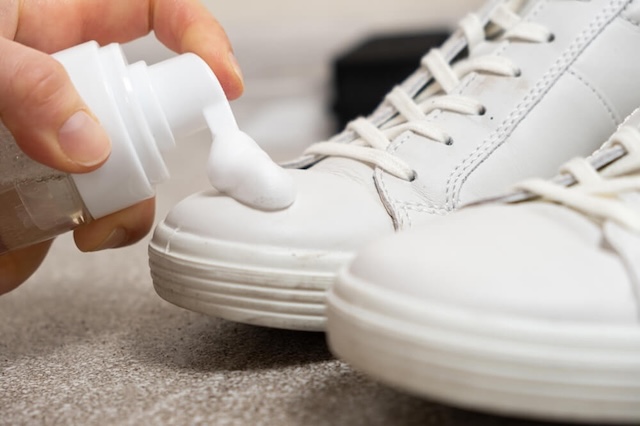 Applying specialized foam cleaner to remove scuffs and stains from a pair of white leather sneakers, a modern twist on classic shoe care