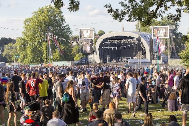 A large crowd gathers at a modern-day Field Day festival, celebrating the evolution of the event from school sports to a full-scale community celebration filled with activities and performances