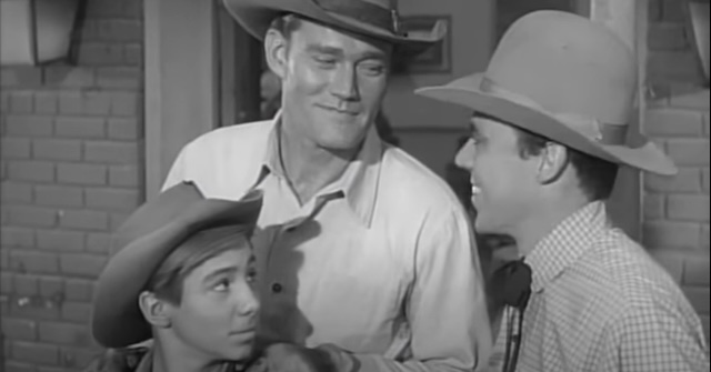 Lucas McCain (Chuck Connors) shares a smile with his son Mark (Johnny Crawford) and a guest in an episode of The Rifleman. Their father-son dynamic was central to the show’s enduring appeal