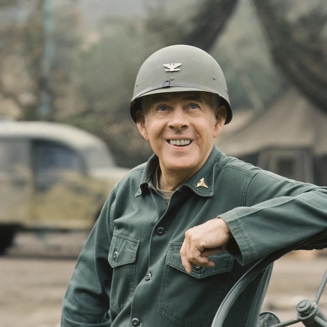 Colonel Potter in M*A*S*H: Harry Morgan as Colonel Sherman T. Potter, proudly smiling in his green army fatigues, representing a figure of leadership and humor in the iconic TV show