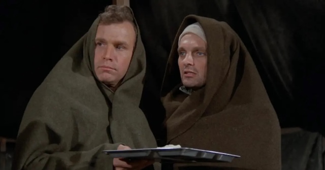 Trapper John (Wayne Rogers) and another soldier wrapped in blankets, highlighting the bitter cold of the Korean War camp in M*A*S*H.