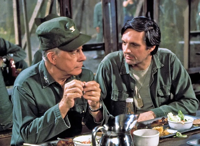 Harry Morgan (Colonel Potter) shares a thoughtful conversation with Alan Alda (Hawkeye Pierce) over a meal at the mess hall, capturing a reflective moment between two commanding officers on M*A*S*H.