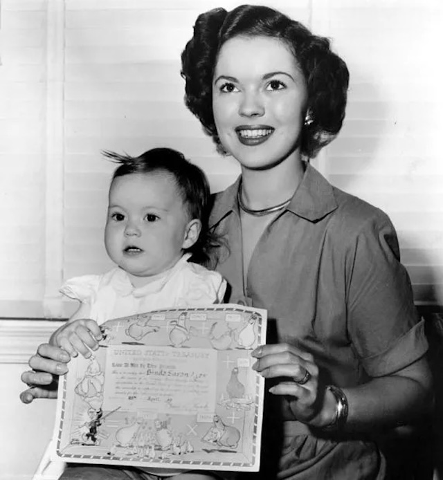 A proud moment captured as Shirley Temple, now a young mother, presents her daughter Linda’s birth certificate, reflecting on a new chapter in her life.