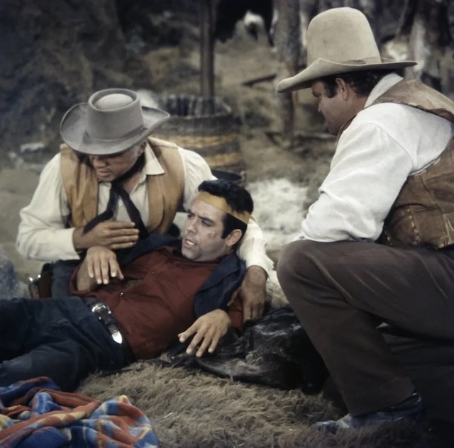 A dramatic moment from Bonanza where Adam Cartwright is injured and being tended to by Ben and Hoss. The concern on their faces shows the close bond between the family members