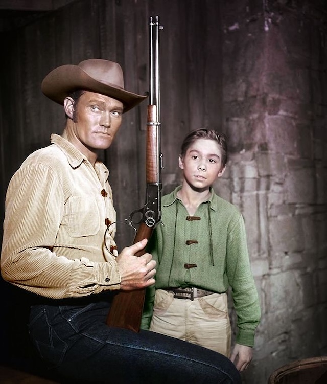 Lucas McCain, the "Rifleman," stands with his iconic Winchester rifle alongside his son Mark. Chuck Connors and Johnny Crawford defined classic Western TV with their compelling portrayal of a father and son navigating life in the Old West.