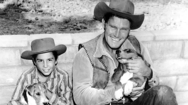 Johnny Crawford and Chuck Connors sharing a light moment with their beloved dogs during the filming of the popular Western series