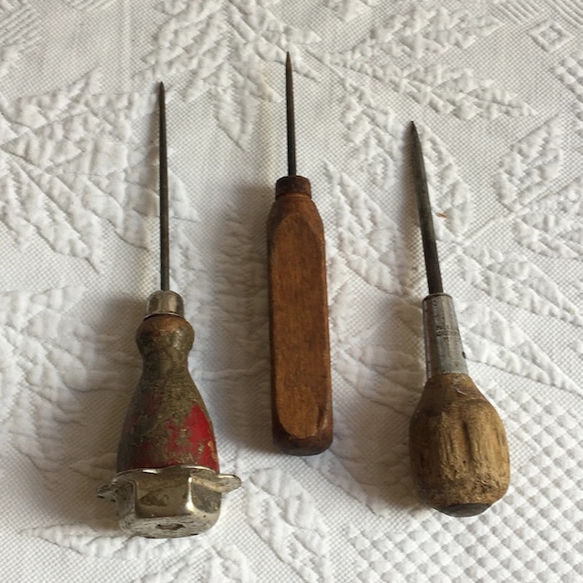 Three unique vintage awls, each with a distinct handle design, resting side-by-side