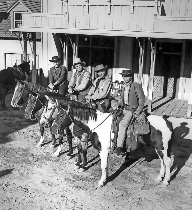 The Bonanza cast mounted on their horses in front of a rustic building, exuding Western charm