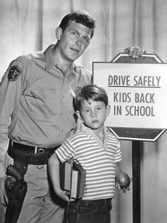 Andy Taylor (Andy Griffith) and Opie (Ron Howard) posing for a promotional photo encouraging safe driving as kids head back to school, showcasing their father-son relationship on The Andy Griffith Show