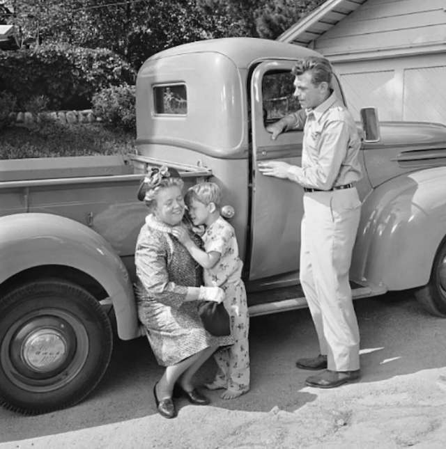 Opie hugs Aunt Bee goodbye while Andy looks on fondly, a tender scene capturing the tight-knit family relationships in Mayberry