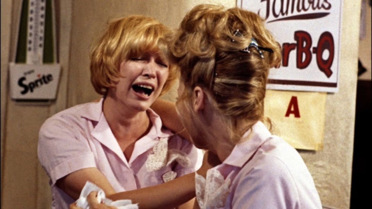 An emotional moment between waitresses Flo (Polly Holliday) and Alice (Linda Lavin) in the kitchen of Mel's Diner, showcasing the strong bonds and dramatic moments behind the show's comedic exterior