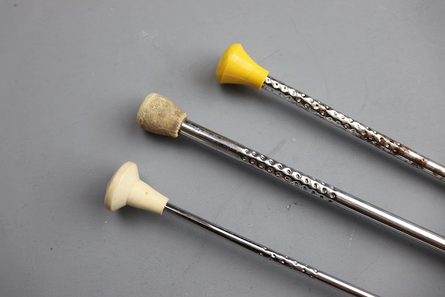 Three vintage twirling batons with different grip styles, each representing a slightly different era in baton twirling. The chrome finish and plastic tips have remained largely unchanged, preserving their nostalgic look