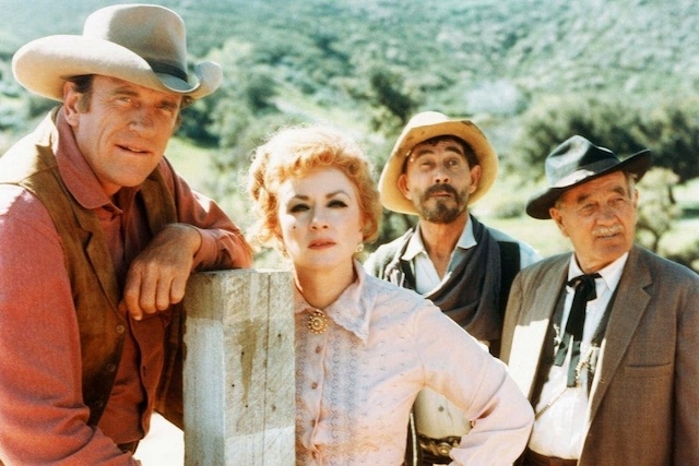 James Arness as Marshal Dillon, Amanda Blake as Miss Kitty, Ken Curtis as Festus, and Milburn Stone as Doc Adams—the heart and soul of Gunsmoke—in a candid moment on set.