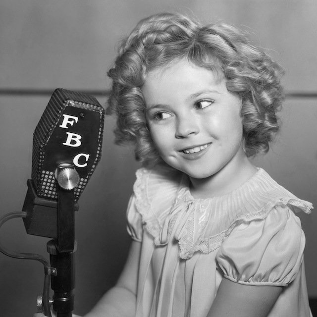 Shirley Temple stands next to a radio microphone, embodying the voice that entertained millions, even beyond the movie screen