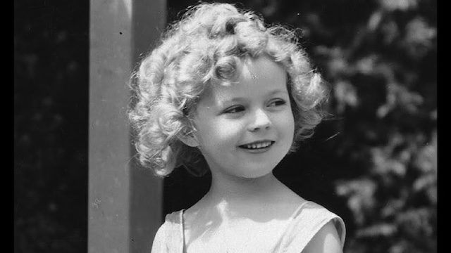 Shirley Temple, at the peak of her child stardom, with her signature curls and smile, capturing hearts across the globe during the 1930s