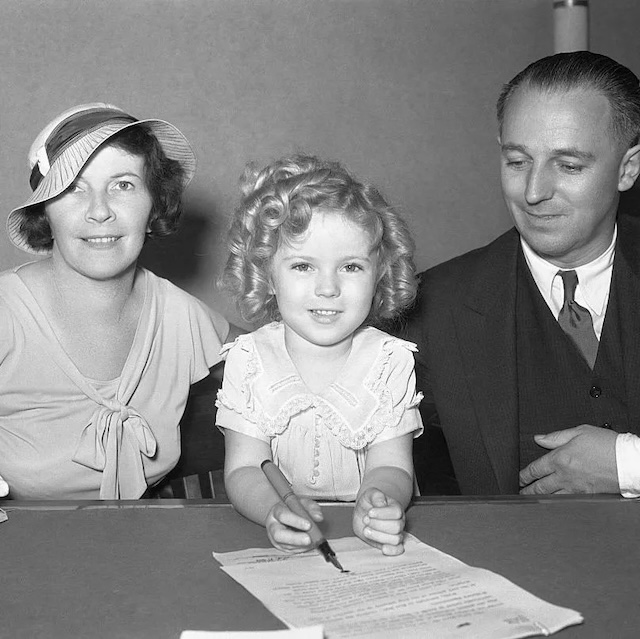 Shirley signs a document as her parents, George and Gertrude, look on