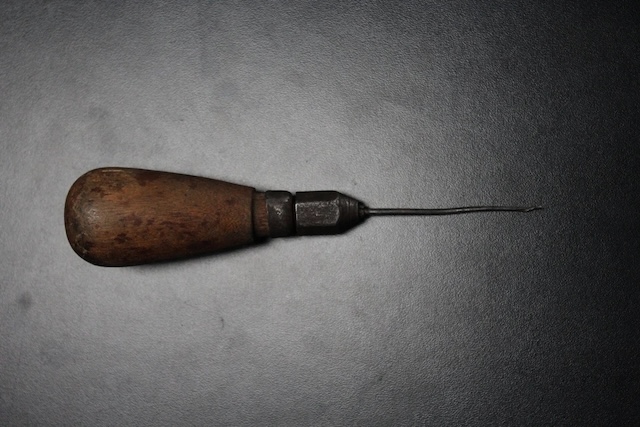 A weathered vintage awl lying against a dark background, highlighting its rustic charm