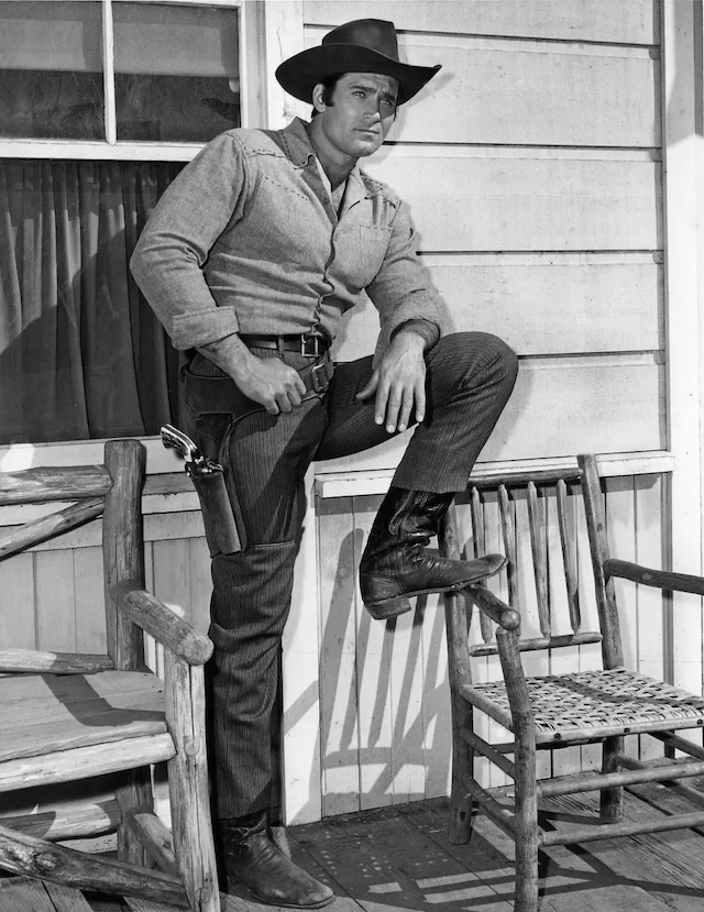 Clint Walker in a commanding pose on a porch - A still that captures Walker’s imposing presence as a Western star.