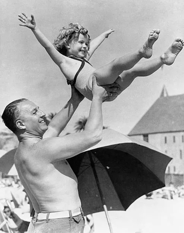 George Temple playfully lifts Shirley at the beach, a glimpse of their family life