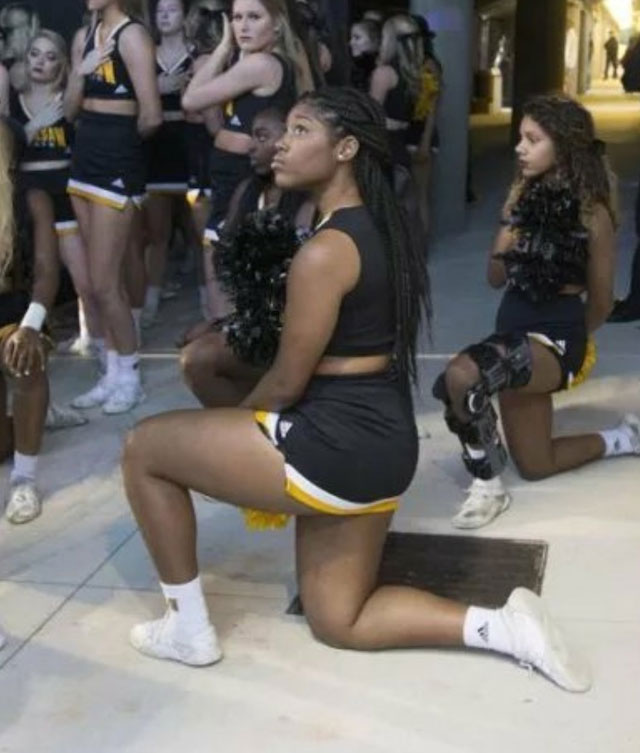 Cheerleaders kneel backstage as they prepare to take the field, a quiet yet powerful gesture in support of racial equality and social justice movements.