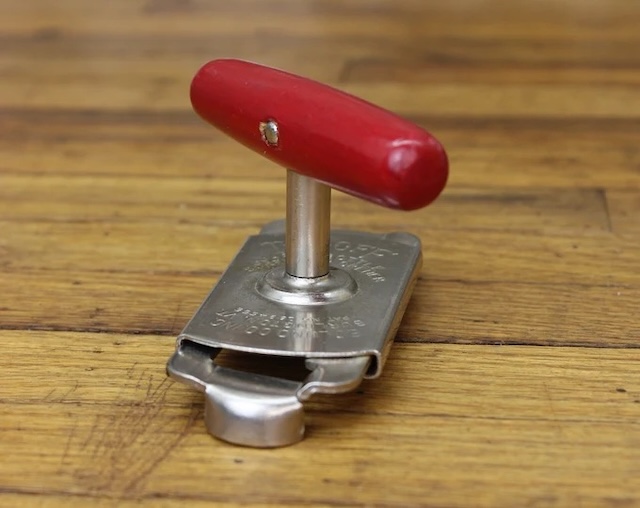 This vintage jar opener features a vibrant red handle and a sturdy metal clamp, a reliable tool from kitchens of the past.