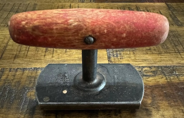 A well-worn vintage jar opener with a faded red handle, carrying the marks of years of use in the kitchen.