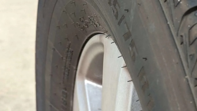 A side view of a car tire, highlighting the presence of vent spews or tire whiskers, commonly found on freshly manufactured tires.