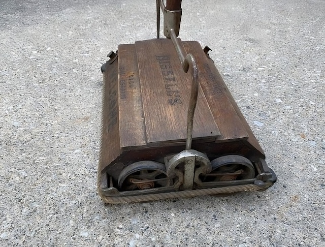 This image showcases the wooden body of an old vintage carpet sweeper, giving a glimpse into the sturdy and practical design of early 20th-century cleaning tools.