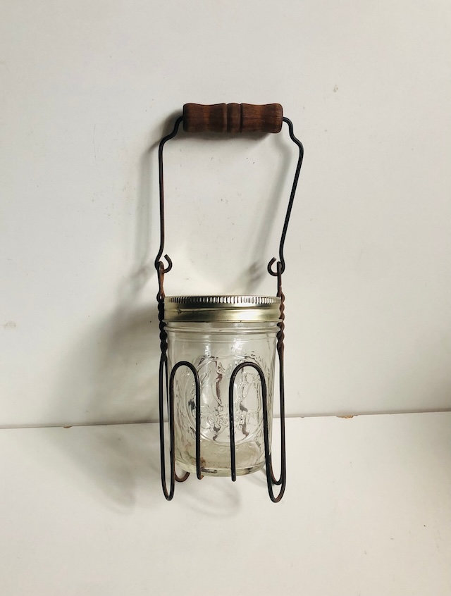 A wooden-handled vintage canning jar lifter holding a sealed jar, a key tool for home preservation in past decades