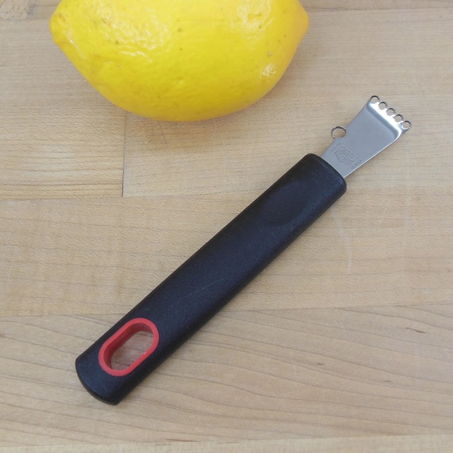 A vintage fruit zester placed next to a fresh lemon, emphasizing its practical use for zesting citrus fruits