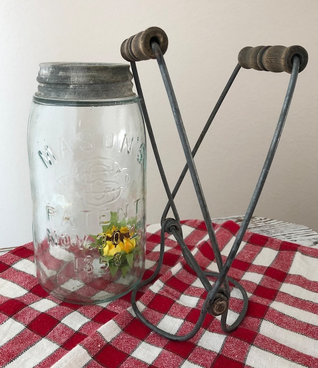 A vintage mason jar lifter beside a Mason jar, symbolizing traditional canning methods