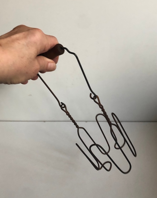 A hand gripping a well-worn vintage canning jar lifter, a useful tool from an earlier era