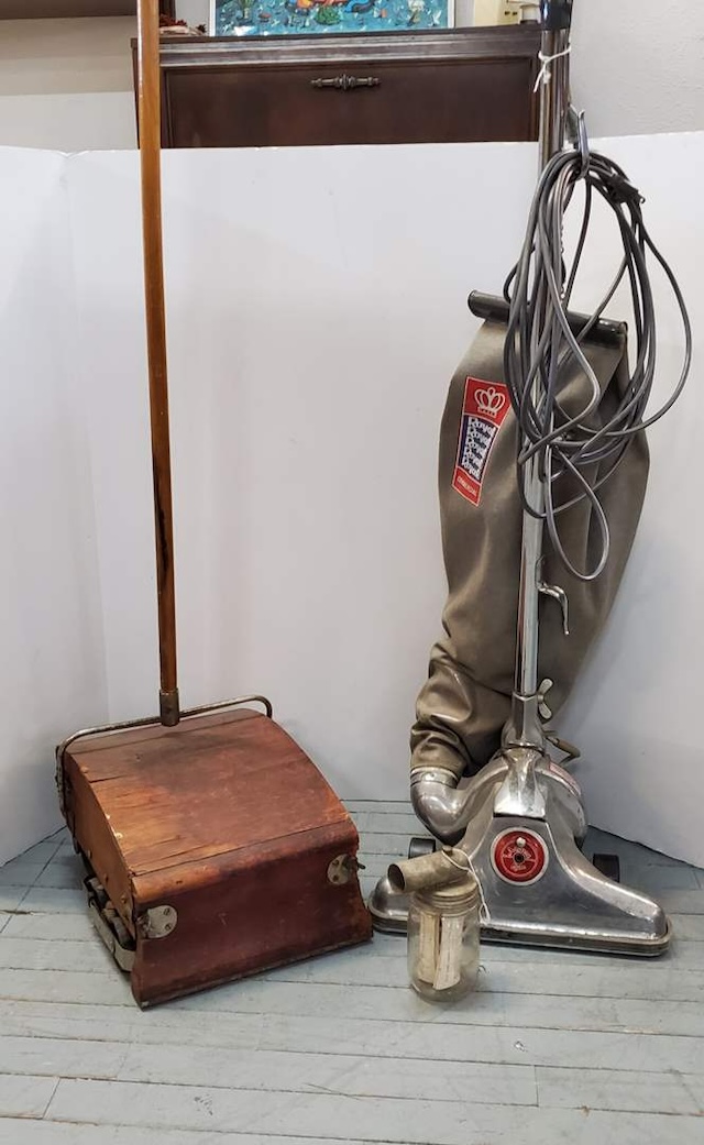 The contrast between the vintage carpet sweeper and a more modern vacuum cleaner in this image highlights the evolution of cleaning technology over the years.