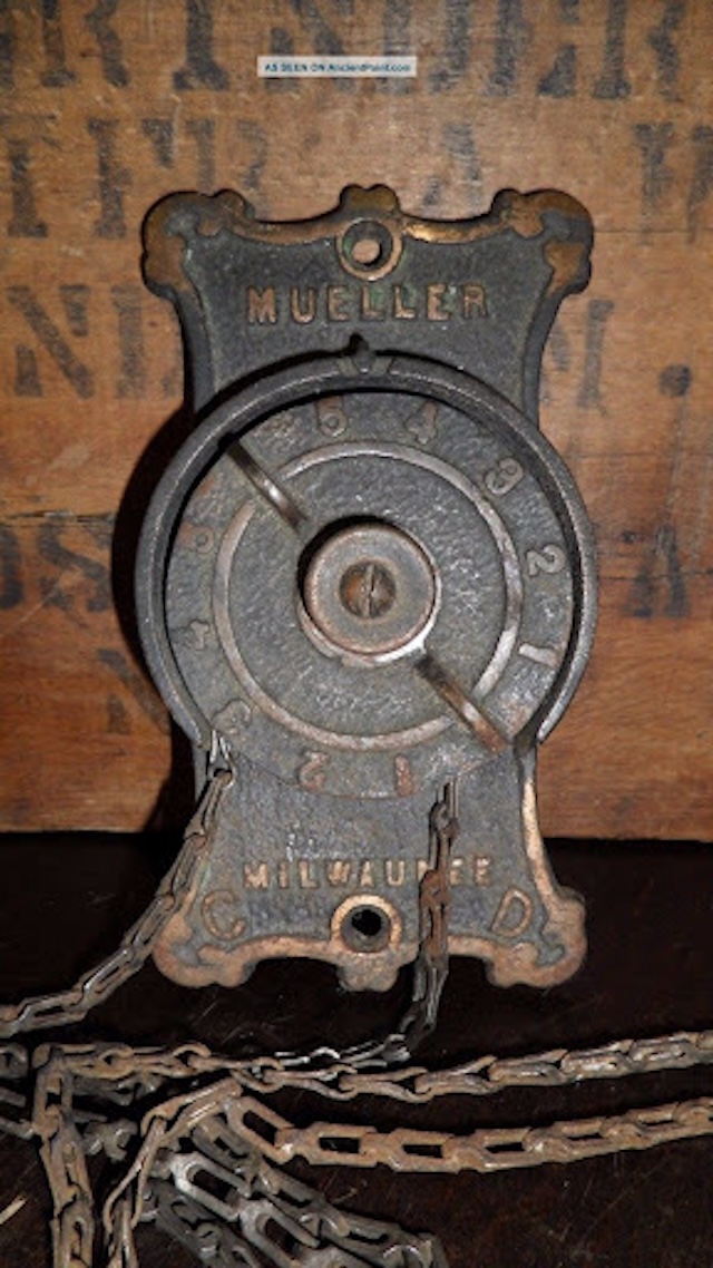 A view of the antique furnace dial plate attached to its original chains, highlighting its mechanical functionality.