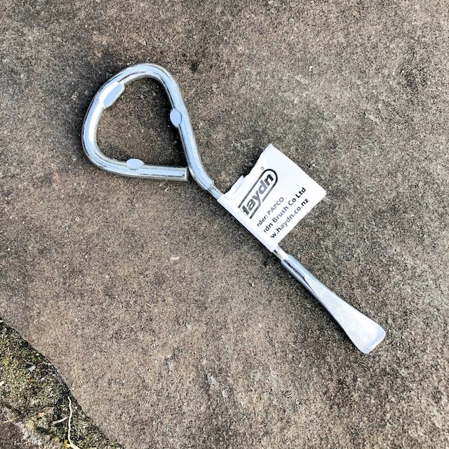 A shiny, almost pristine paint can opener lying on rough concrete, a nod to its rugged, durable nature