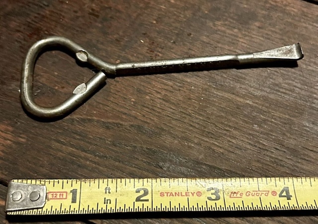 A well-worn paint can opener measured against a ruler, highlighting its compact, portable design