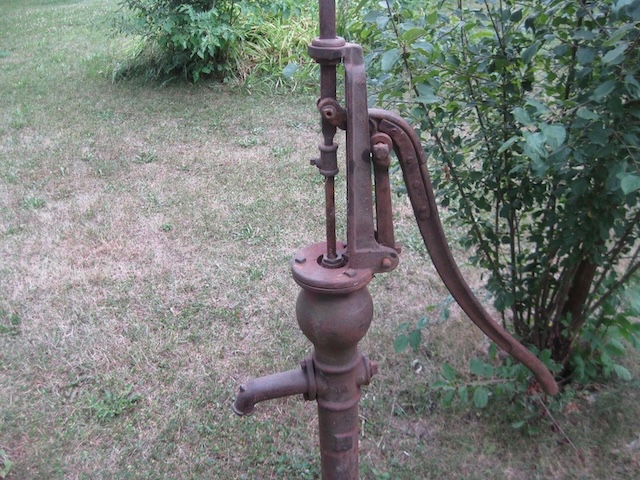 A vintage Fairbury hand pitcher pump standing tall in the garden, a relic from the days when water was drawn by hand.