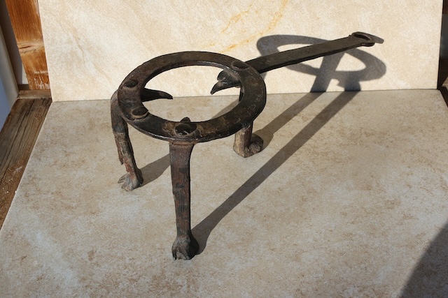 A brass-decorated vintage trivet featuring a lyre-shaped design, often used in more upscale homes where style was as important as function