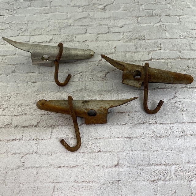 Three vintage spiles with hooks laid against a textured background, showing their rugged build and unique design, used for collecting sap from trees