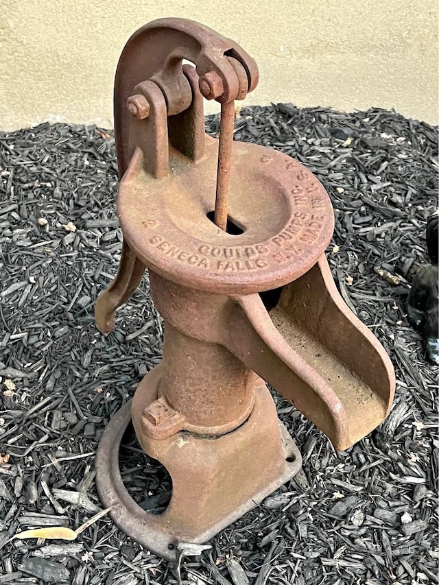 A close-up of a classic Fairbury hand pump, its rusted body a testament to the robust engineering of a bygone time.