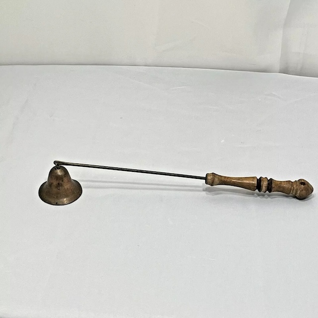 Rustic Brass Candle Snuffer on White Cloth – This antique brass candle snuffer with a beautifully aged wooden handle carries the stories of many candlelight evenings, still functional for those who cherish tradition.