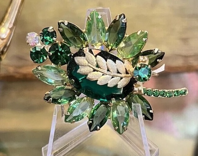 A striking Juliana D&E vintage jewelry brooch with a mix of deep green and light green rhinestones, accented by a delicate leaf motif, exemplifying the artistry of the era.