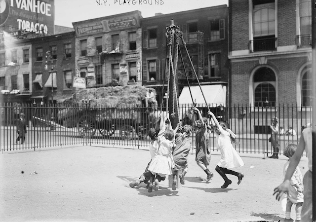 A simple but exciting rope swing entertains a group of children in a New York playground, surrounded by the city's bustling streets and tall buildings