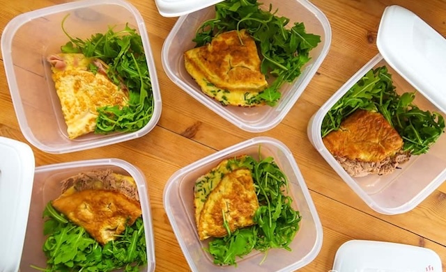 Individual omelets with fresh greens are portioned out and ready for freezing, offering a healthy, quick breakfast solution