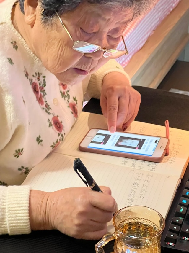 Carefully jotting down notes from her smartphone, this grandmother's dedication to mastering video editing reflects her lifelong commitment to learning